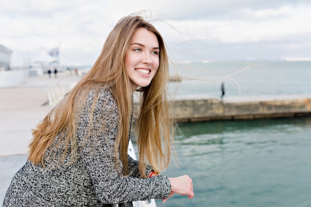 Heureuse belle femme avec de longs cheveux brun clair et de grands yeux bleus riant et se promène près de la mer