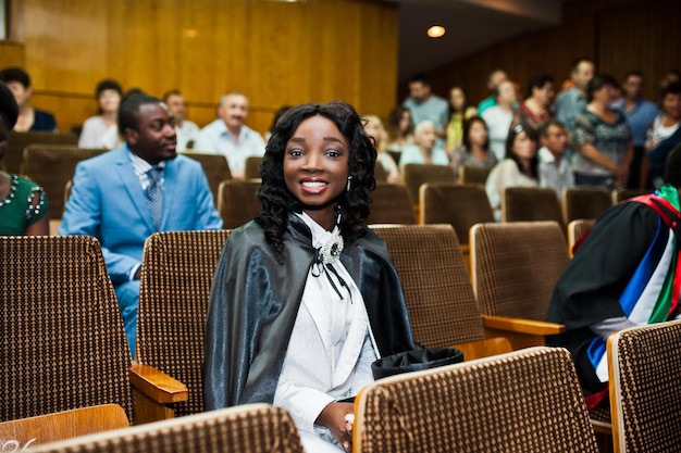 Heureuse belle fille afro-américaine noire avec chapeau et robe diplômés lors de la cérémonie diplômée