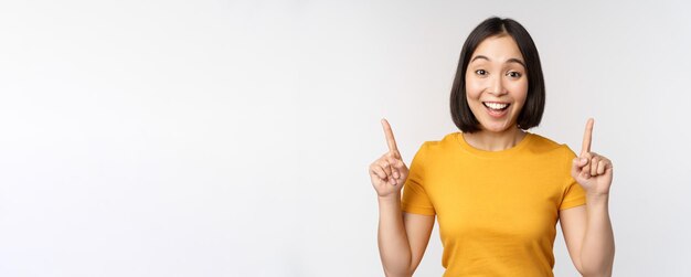 Heureuse belle fille asiatique montrant une publicité pointant du doigt debout sur fond blanc