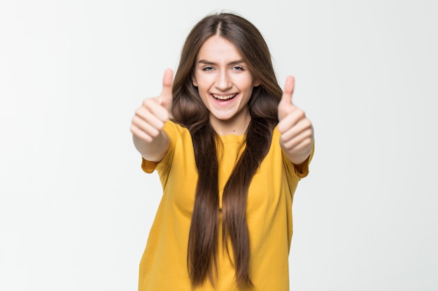 Heureuse belle fille montrant le pouce en l'air symbole par deux mains isolé sur mur blanc