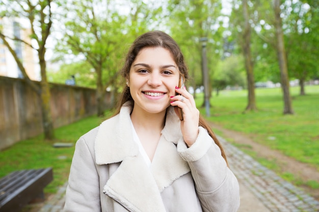 Heureuse belle jeune femme appeler au téléphone dans le parc