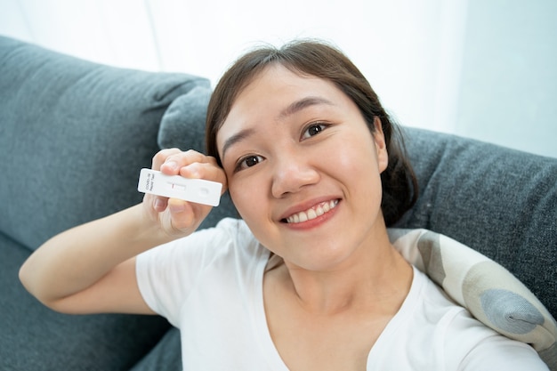 Heureuse belle jeune femme asiatique montrant un résultat négatif du résultat du test de l'antigène covid-19 ou du sras 2019-ncov à la caméra tout en passant un appel vidéo avec sa famille et son médecin. test ag covid-19 à la maison.