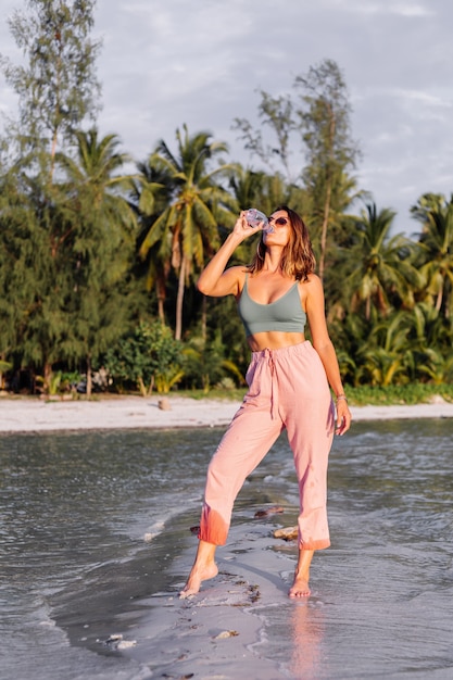 Photo gratuite heureuse belle jeune femme européenne avec une bouteille d'eau en plastique dans sa main sur la plage