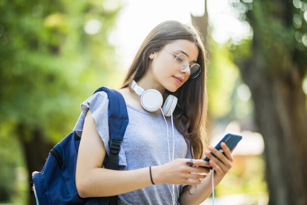 Heureuse belle jeune fille de race blanche avec un téléphone intelligent vert à l'extérieur le jour d'été ensoleillé envoyant des SMS et souriant.