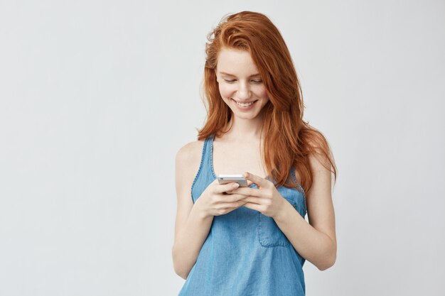 Heureuse belle rousse regardant le téléphone et souriant.