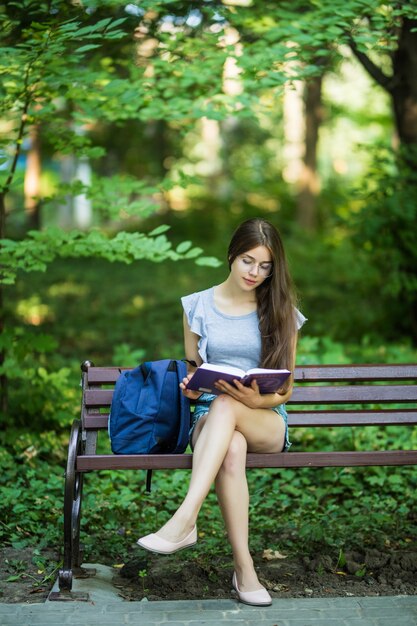 Heureuse brune avec un ordinateur portable en mains assis sur un banc de parc