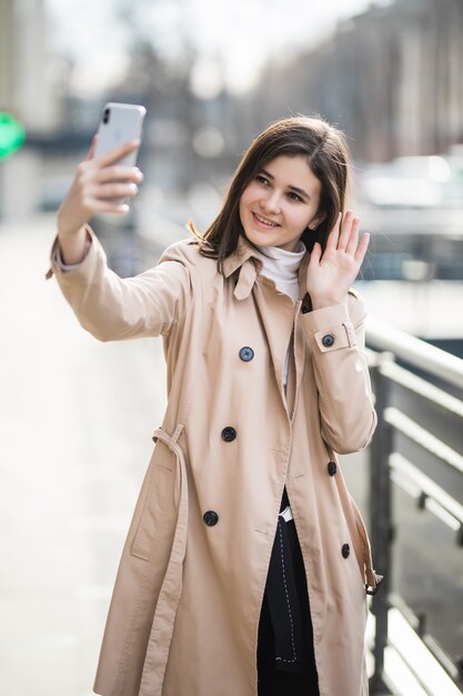 Heureuse brune souriante a un appel vidéo sur son téléphone à l'extérieur