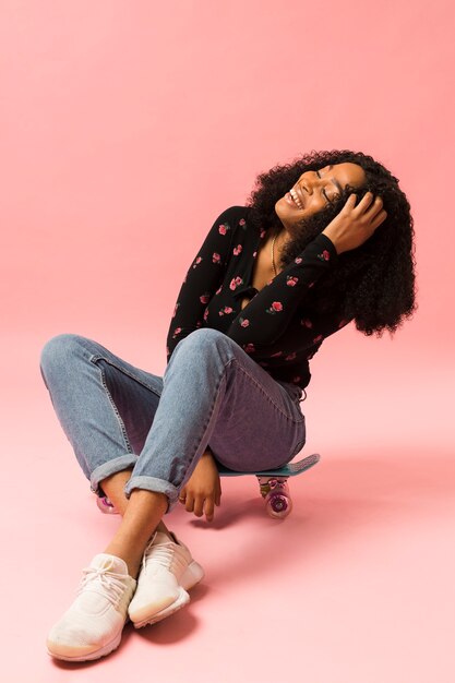 Heureuse dame afro-américaine assise sur une planche à roulettes