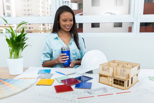 Heureuse dame afro-américaine sur chaise avec ventouse près du plan et modèle de maison sur table