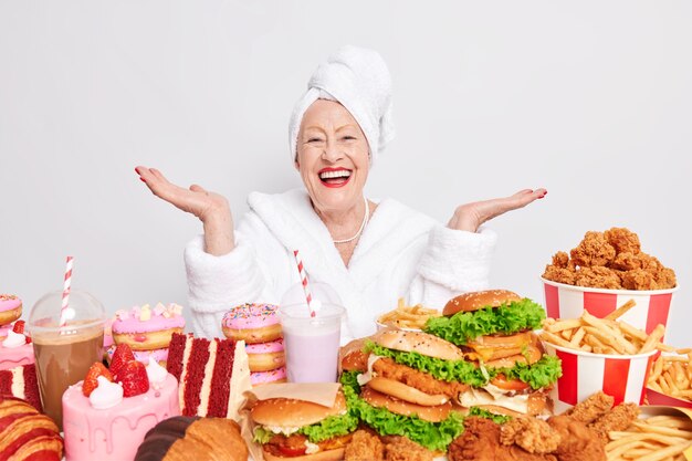 Heureuse dame âgée écarte les paumes se sent heureuse a une nutrition déséquilibrée malsaine mange de la malbouffe