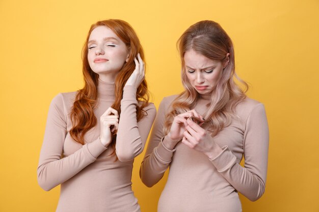 Heureuse dame rousse touchant ses cheveux près de femme blonde triste