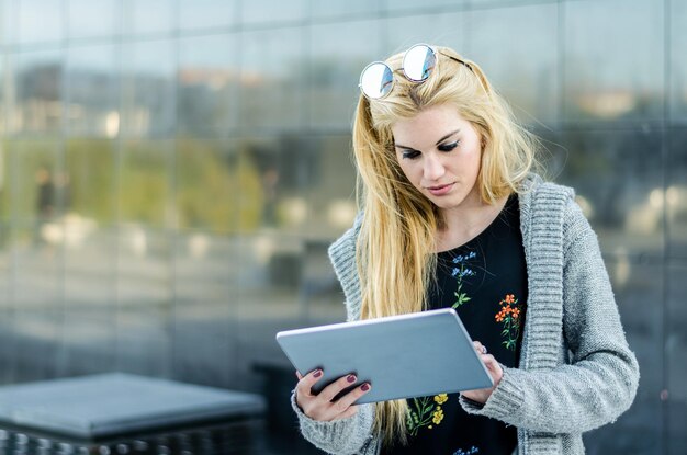 Heureuse étudiante blonde avec tablette dans un mur de réflexion