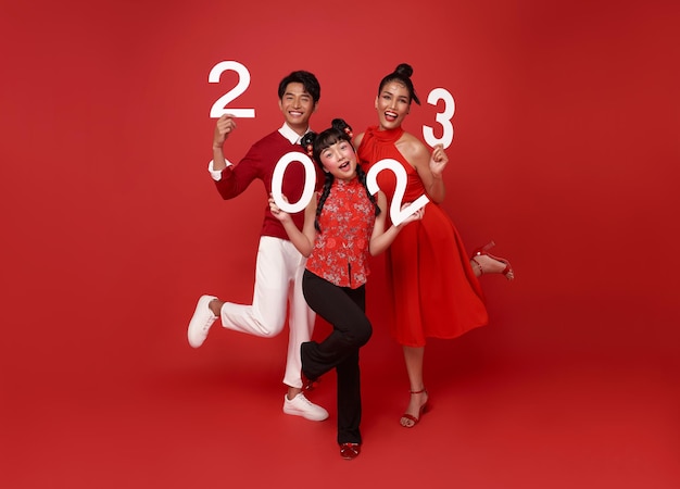 Heureuse famille asiatique en tenue décontractée rouge montrant le numéro 2023 saluant la bonne année
