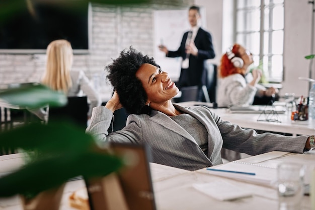 Photo gratuite heureuse femme d'affaires afro-américaine prenant une pause du travail et rêvant au bureau il y a des gens en arrière-plan