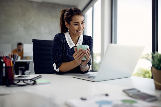 Heureuse femme d'affaires faisant un appel vidéo sur un ordinateur portable pendant sa pause-café au bureau