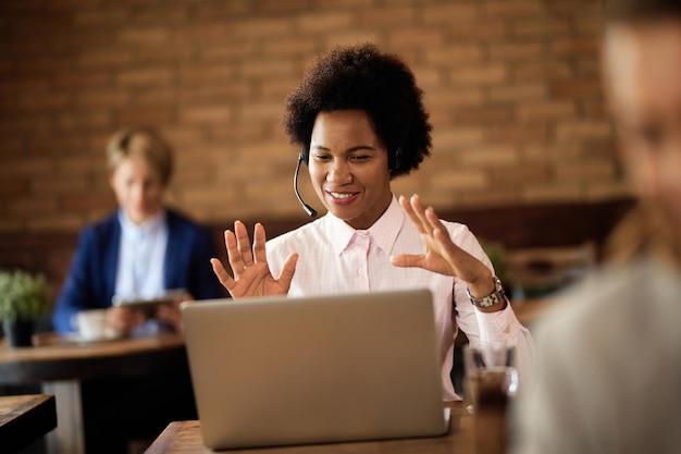 Heureuse femme d'affaires noire faisant un appel vidéo sur un ordinateur portable dans un café