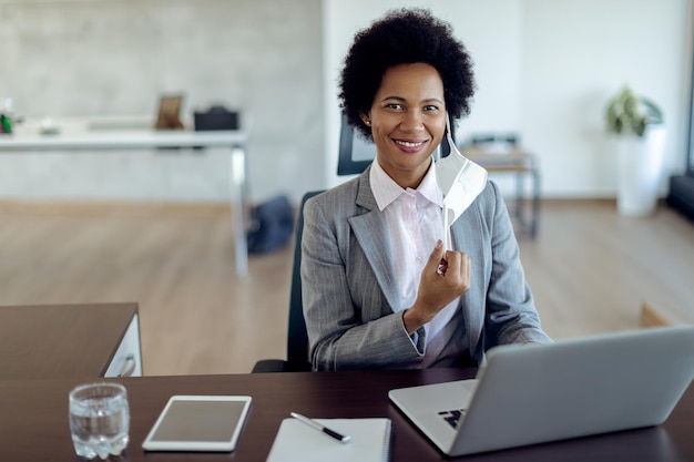 Heureuse femme d'affaires noire avec masque protecteur travaillant au bureau