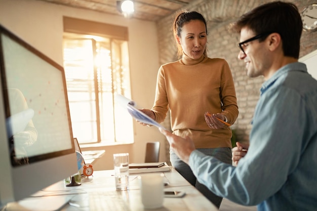 Heureuse femme d'affaires parlant à son collègue tout en analysant des rapports au bureau