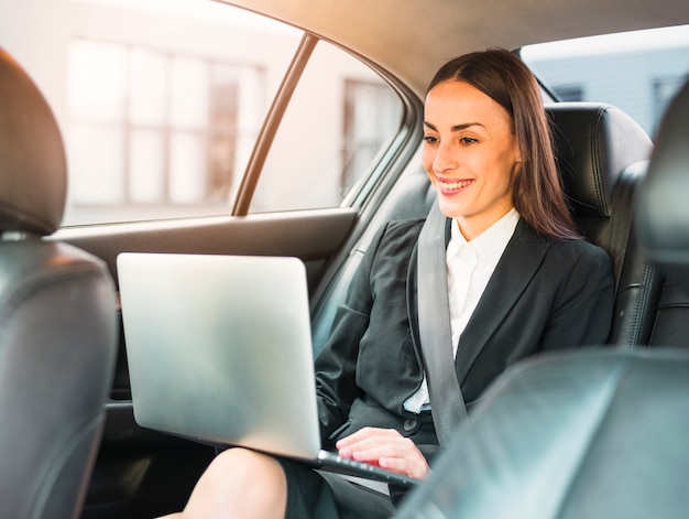 Heureuse femme d&#39;affaires voyageant en voiture à l&#39;aide d&#39;un ordinateur portable