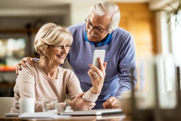 Heureuse femme âgée utilisant un téléphone portable avec son mari à la maison
