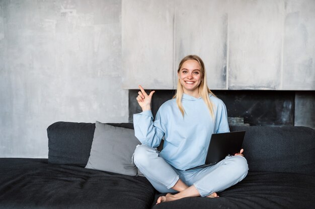 Photo gratuite heureuse femme à l'aide d'un ordinateur portable argenté assis sur un canapé