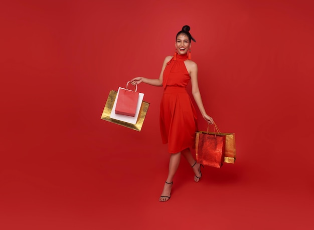 Heureuse femme asiatique accro du shopping portant une robe rouge tenant un sac à provisions à pied du centre commercial