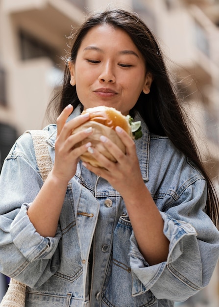 Heureuse femme asiatique, manger un hamburger à l'extérieur