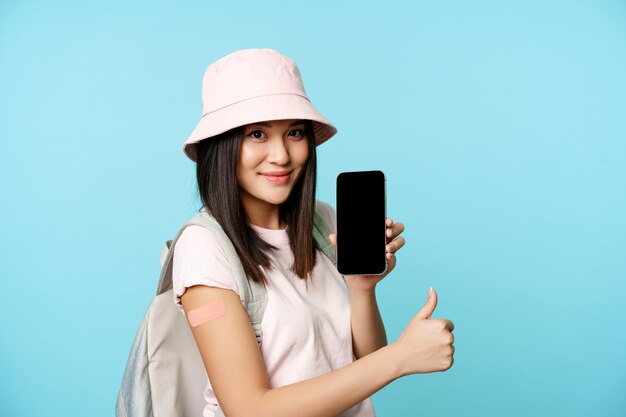 Heureuse femme asiatique montrant un passeport de santé sur l'écran du téléphone portable main vaccinée avec les pouces de patch u...