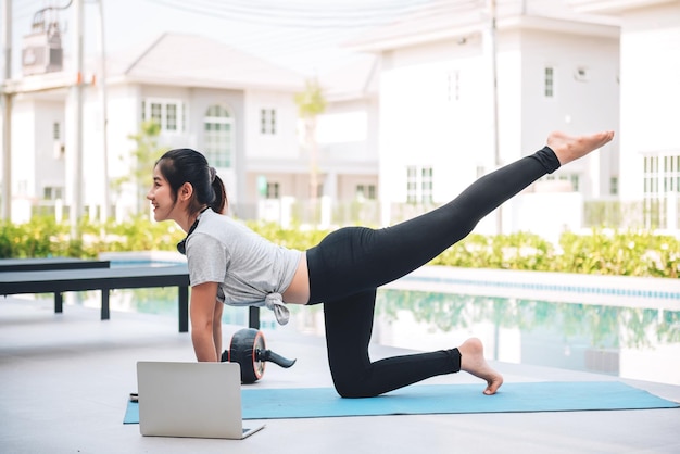 Heureuse femme asiatique qui s'étend de l'exercice et de l'entraînement de yoga le matin à la maison en plein air