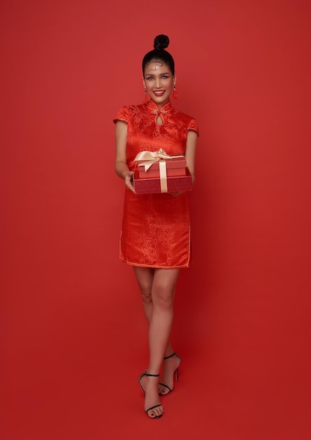 Heureuse femme asiatique souriante en costume traditionnel rouge donnant une boîte cadeau pour bénir le nouvel an chinois