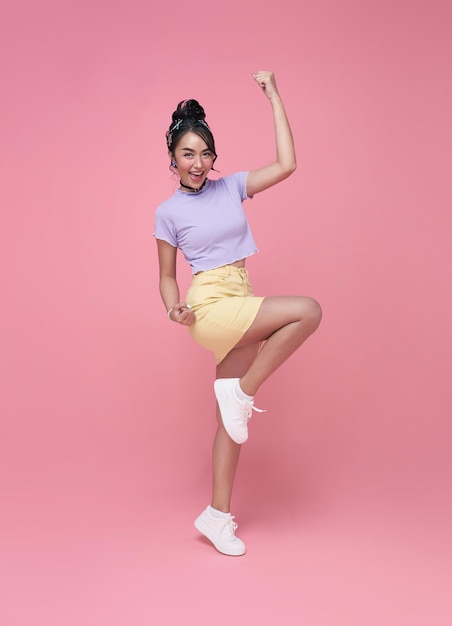 Heureuse femme asiatique souriante et sautant tout en célébrant le succès isolé sur fond rose