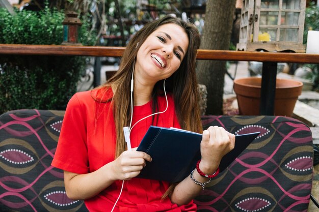 Heureuse femme assise sur un canapé avec agenda en écoutant de la musique sur des écouteurs