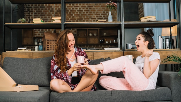 Photo gratuite heureuse femme assise sur un canapé en cochant les pieds de son amie