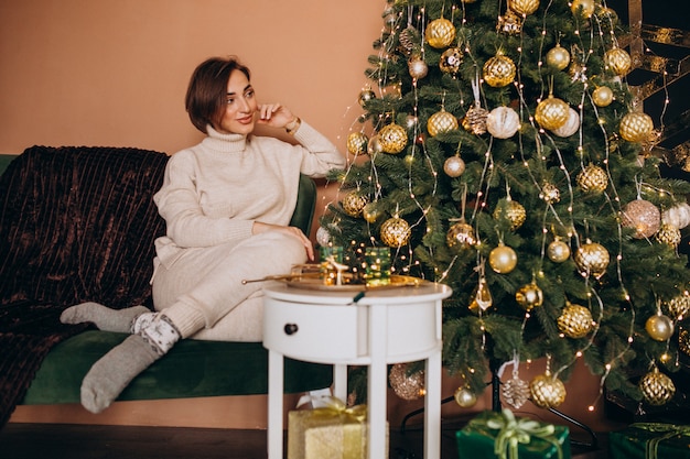 Heureuse femme assise sur un canapé près de l'arbre de Noël