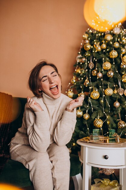 Heureuse femme assise sur un canapé près de l'arbre de Noël