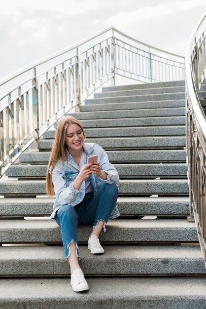 Heureuse femme assise sur des escaliers et à l&#39;aide de smartphone