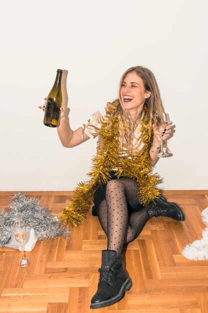 Heureuse femme assise sur le sol avec une bouteille de champagne