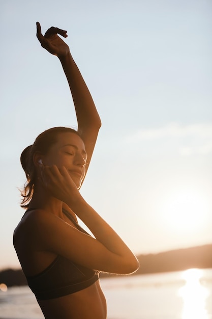 Photo gratuite heureuse femme athlétique écoutant de la musique et appréciant les yeux fermés au bord de la rivière le matin