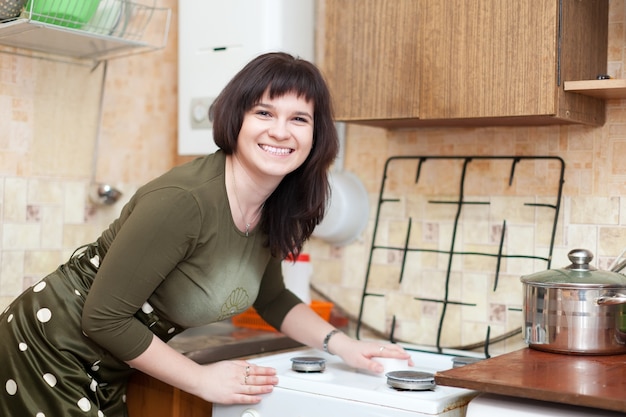 Heureuse femme au foyer nettoie la cuisinière à gaz avec une éponge de mélamine