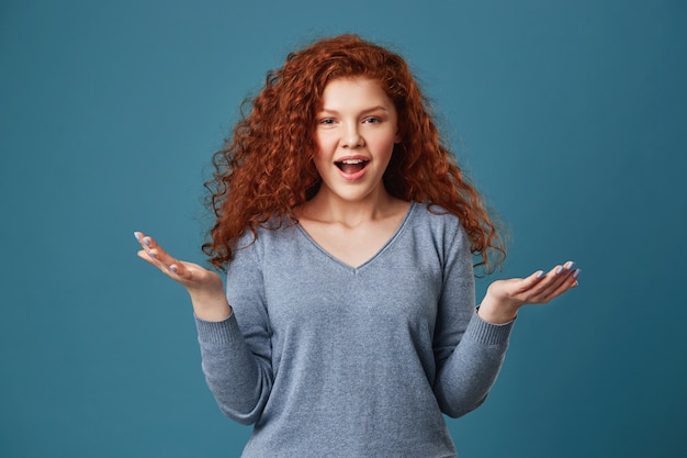 Heureuse femme au gingembre avec des taches de rousseur en chemise grise écartant les mains, étant heureuse surprise quand la mère a donné son cadeau d'anniversaire.