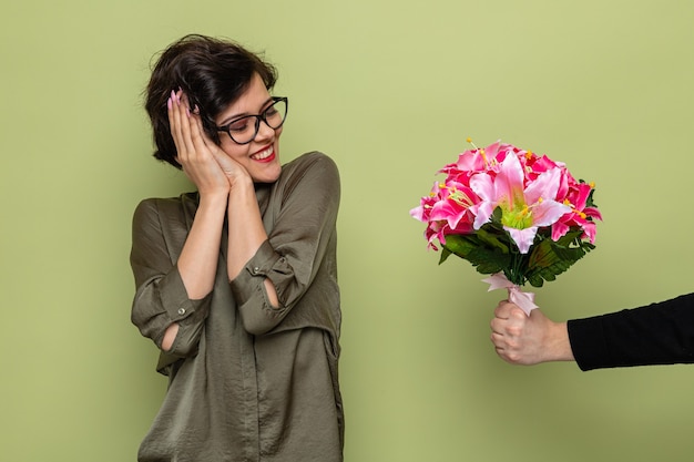 Heureuse femme aux cheveux courts à la surprise et heureux souriant joyeusement tout en recevant un bouquet de fleurs de son petit ami célébrant la journée internationale de la femme le 8 mars