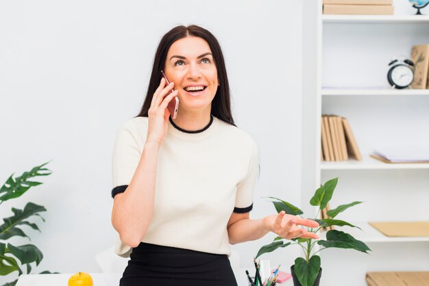 Heureuse femme en blanc parlant par téléphone au bureau