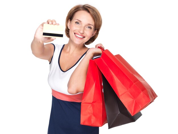 Heureuse femme blanche avec des sacs à provisions et une carte de crédit sur un mur blanc