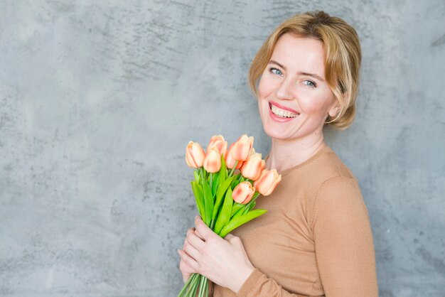 Heureuse femme blonde debout avec bouquet de tulipes