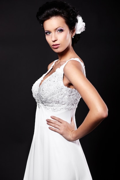 Heureuse femme brune belle mariée sexy en robe de mariée blanche avec coiffure et maquillage lumineux