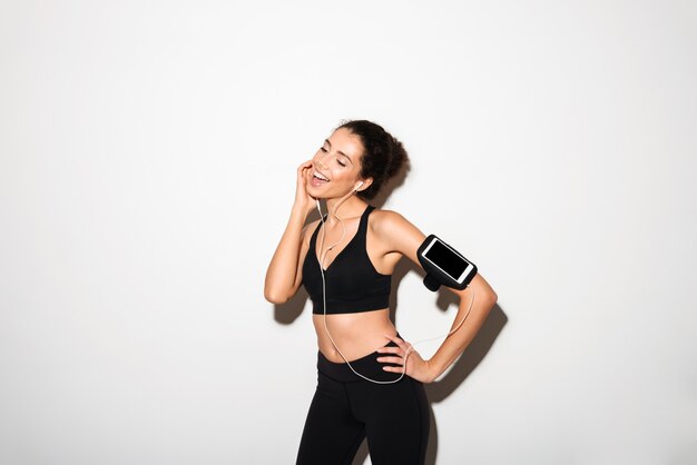 Heureuse femme brune bouclée de remise en forme, écouter de la musique par smartphone