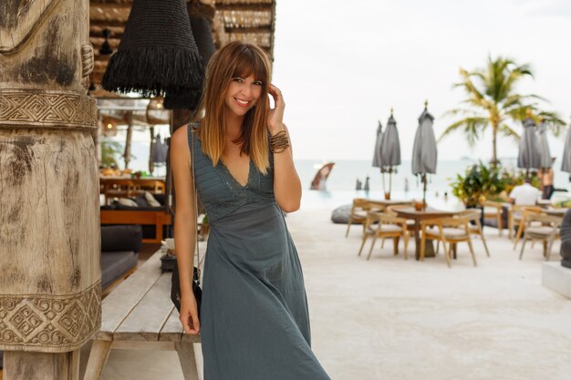 Heureuse femme brune en robe sexy posant dans un restaurant de plage élégant dans un style asiatique.