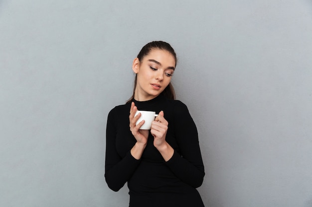 Heureuse femme brune en vêtements noirs tenant une tasse de café