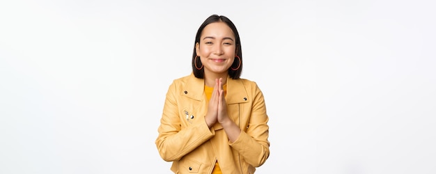 Heureuse femme coréenne à la recherche d'espoir demandant de l'aide en faveur de la mendicité debout avec un geste de namaste et souriant debout sur fond blanc