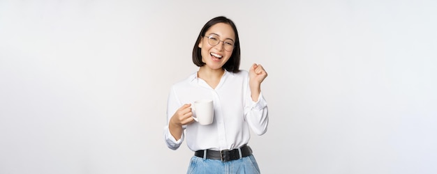 Heureuse femme dansante buvant du café ou du thé à partir d'une tasse fille coréenne avec une tasse debout sur fond blanc